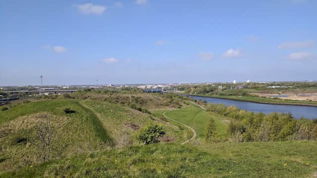 Lush green hills overlook a winding river, with a clear blue sky and distant buildings in the background.