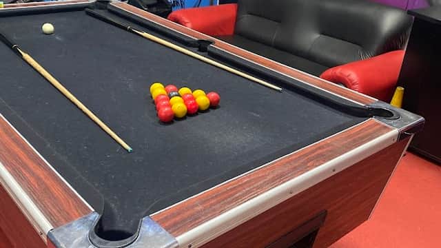 Pool table with colored balls arranged, red leather sofa, and a TV in a vibrant, modern garage setting.