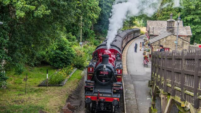 Steam train at Haworth station, surrounded by lush greenery and historic buildings, with passengers waiting nearby.