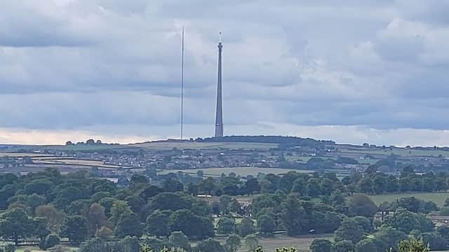 View from car park showing green fields, trees, and a tall radio tower against a cloudy sky in West Bretton, Yorkshire.