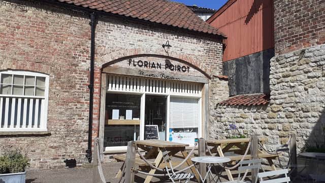Historic brick building with a sign for "Horian Boiot," outdoor seating, and a sunny courtyard in Old Malton.
