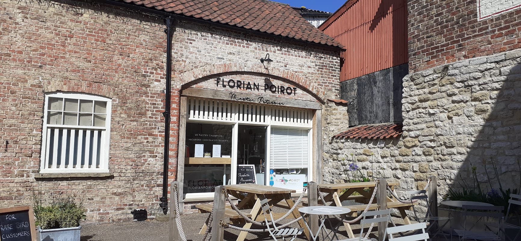 Historic brick building with a sign for "Horian Boiot," outdoor seating, and a sunny courtyard in Old Malton.