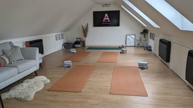 Yoga studio with mats arranged on wooden floor, cozy seating area, and a screen displaying "Abbi Santosha Yoga."