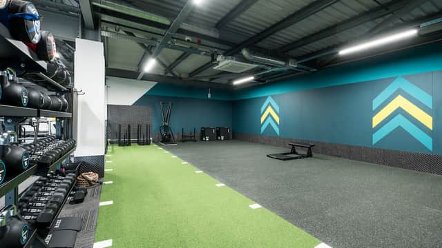Modern gym interior with turf flooring, weights, and workout equipment against vibrant teal and yellow walls.