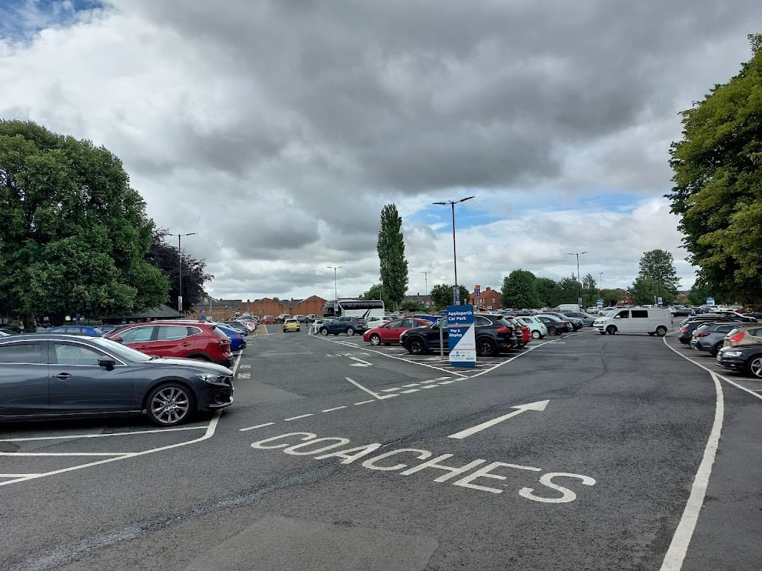 Parking lot with cars and coaches, surrounded by trees under a cloudy sky in Northallerton, Yorkshire.