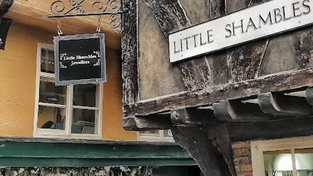 Historic timber-framed buildings along a narrow street, with a jewellers' shop and visitors exploring the area.