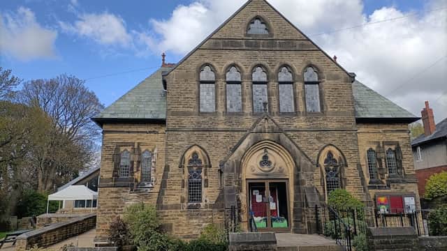 Historic stone church with a pointed arch entrance, surrounded by greenery and a community cafe to the side.