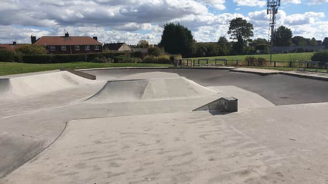 Concrete skatepark features ramps and bowls under a partly cloudy sky, surrounded by grass and houses in Maltby.