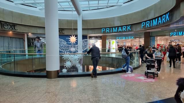 Interior view of Meadowhall shopping center featuring stores like Primark and Next, with shoppers and a stroller.