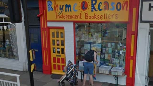 Brightly painted storefront of Rhyme & Reason bookshop with colorful signage, featuring a display of books and a family outside.