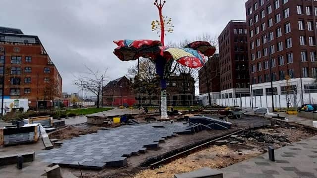 Colorful tree sculpture surrounded by construction materials and buildings in Leeds, Yorkshire under a cloudy sky.