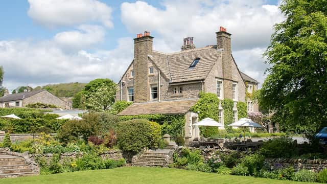 Historic stone venue surrounded by lush gardens and trees, with outdoor seating and a bright blue sky overhead.