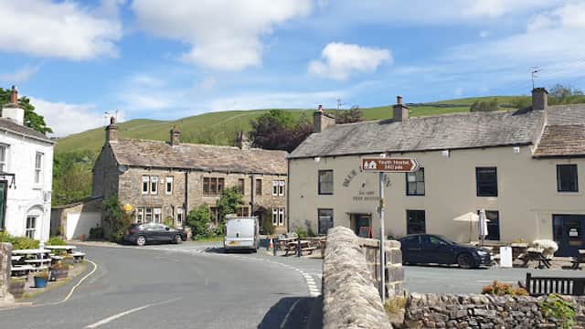 Charming Bed & Breakfast with stone buildings, outdoor seating, and scenic hills under a blue sky in Kettlewell, Yorkshire.