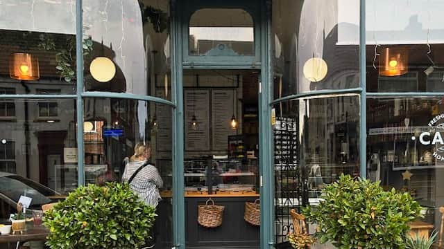 Charming cake shop entrance with large windows, potted plants, and a welcoming sign in Patrington, Yorkshire.