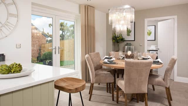Modern dining area with a round wooden table, plush chairs, a chandelier, and sliding doors leading to a garden.