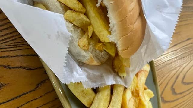 A tray with a sandwich filled with chips and a side of golden fries, accompanied by a glass of orange drink.