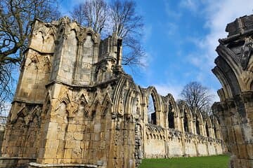 Medieval stone ruins with arched windows and trees, set against a bright blue sky.