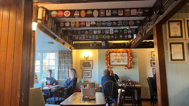 Cozy bar interior with wooden beams, patrons at tables, and a ceiling adorned with beer pump clips.