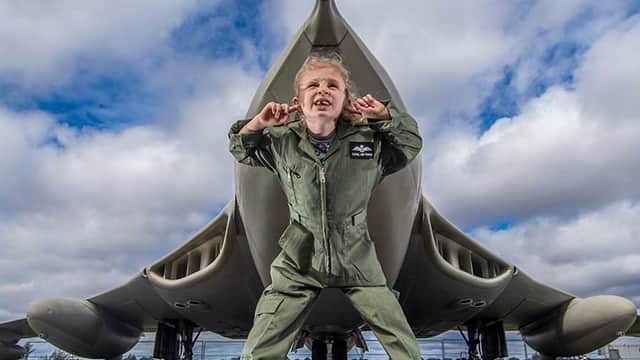 Child in a flight suit stands playfully in front of a large aircraft at the Yorkshire Air Museum.
