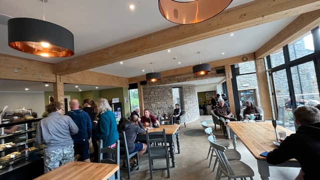 Modern café interior with wooden beams, tables, and customers enjoying food and drinks in a cozy atmosphere.