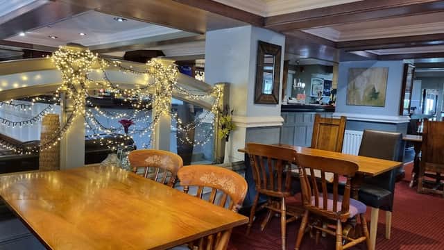 Cozy pub interior with wooden tables, chairs, and festive lights, featuring a bar and artwork on the walls.