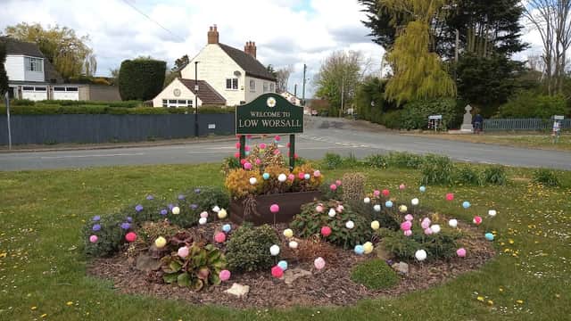 Welcome sign for Low Worsall surrounded by colorful flower beds and greenery on a sunny day.