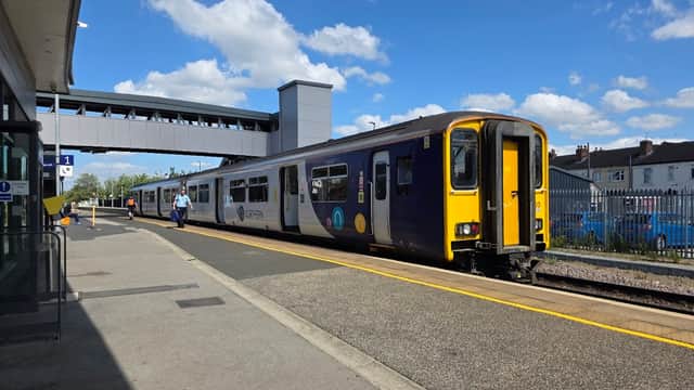 Train at a platform in Castleford, Yorkshire, with a blue sky and clouds overhead, and a pedestrian bridge in the background.