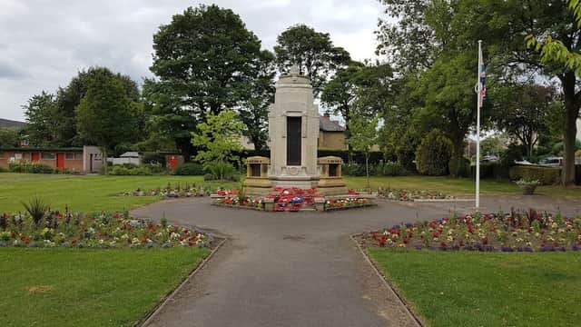 A landscaped park featuring a war memorial, flower beds, and trees under a cloudy sky.