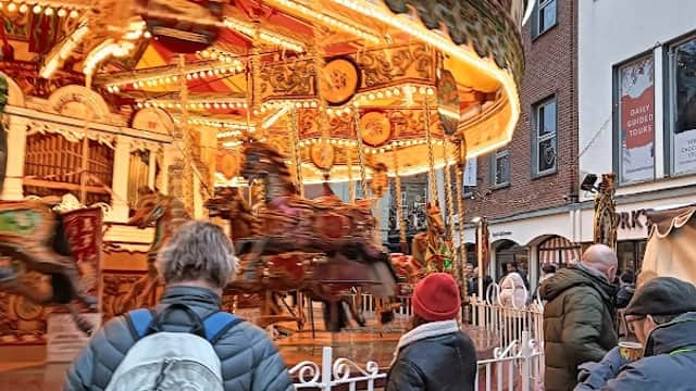 Colorful carousel with lights, people watching, and historic buildings in a lively street scene in York.