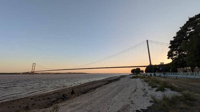 Foreshores East Car Park with a view of the Humber Bridge at sunset, sandy shore, and greenery nearby.