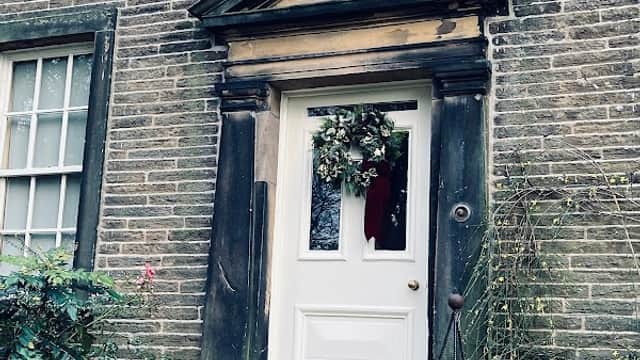 White door with a wreath, stone steps, and greenery beside the entrance of the Brontë Parsonage Museum.