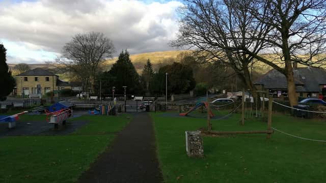 Playground with climbing structures, swings, and benches, surrounded by grass and trees under a cloudy sky in Burtersett.