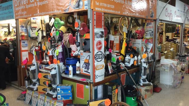 Market stall displaying various vacuum cleaners, appliance spares, and tools, with colorful signage and price tags.
