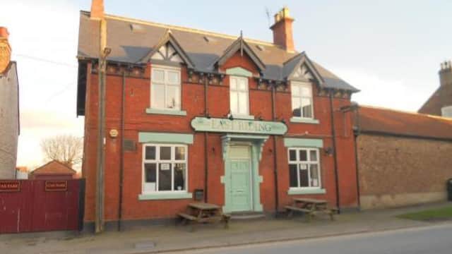 Red brick takeaway with a turquoise sign reading "East Riding," featuring picnic tables outside and a clear blue sky.