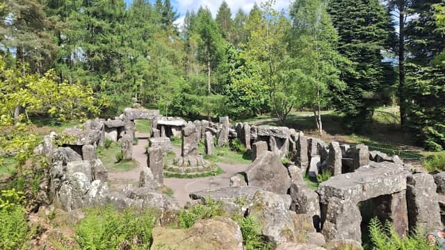 Ancient stone structure surrounded by lush greenery and trees under a blue sky with scattered clouds.