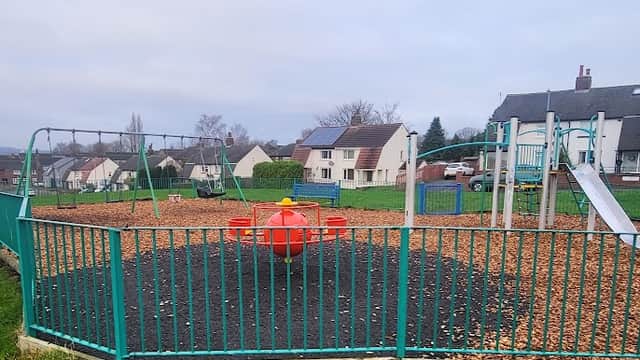 Colorful playground featuring swings, a slide, and a roundabout, surrounded by green grass and houses in the background.