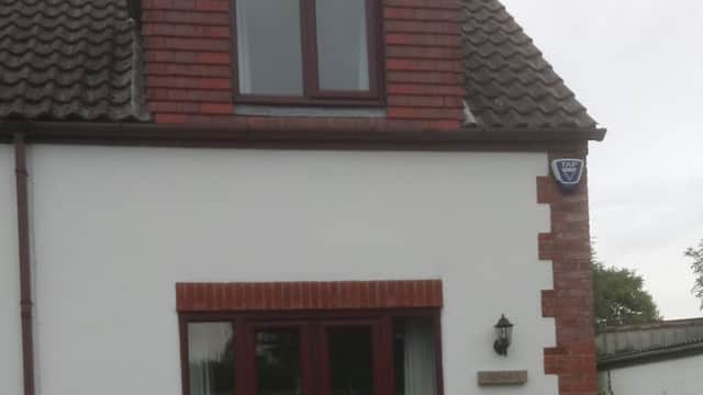 Charming cottage with a red-brick facade, sloped roof, and a parked car in front, set in a rural area.