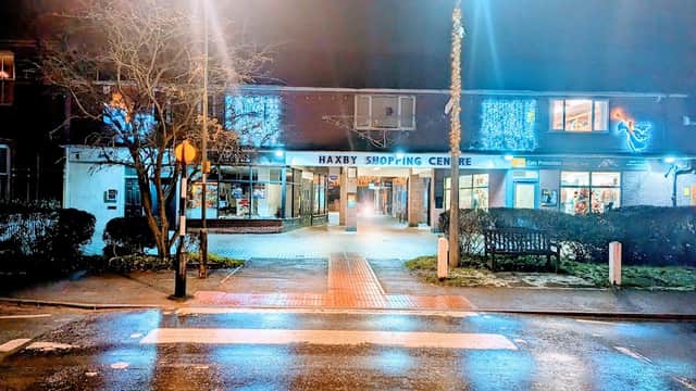 Haxby Shopping Centre entrance illuminated at night, with decorative lights and a wet pavement reflecting the glow.