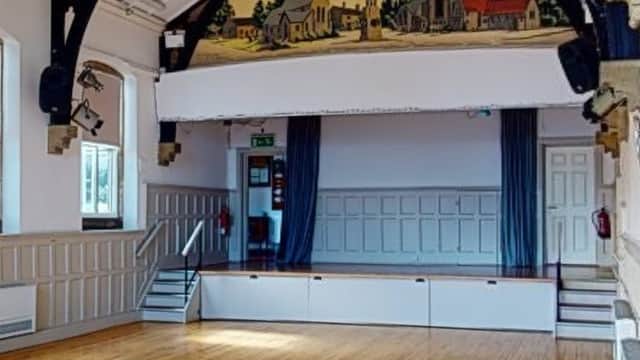 Spacious hall with wooden floor, large stage, and mural of Bramhope village on the ceiling.