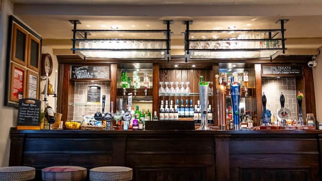 Wooden bar with various bottles, glasses, and taps; chalkboard menus and stools in a cozy pub setting.