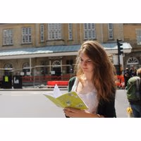 Woman holding a green map booklet for Treasure Hunt Themed City Walking Tours by Curious About, standing outdoors.