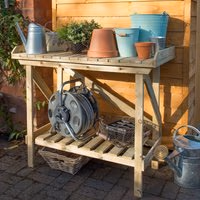 Wooden potting bench with slatted shelf, side supports, and various gardening tools and pots on top.