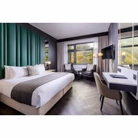Luxury hotel room with king bed, green accent wall, desk, TV, and large windows overlooking greenery.