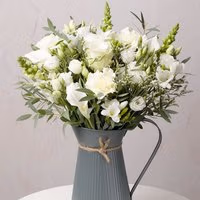 Bouquet of white roses and lisianthus in a gray ribbed metal jug with twine bow.