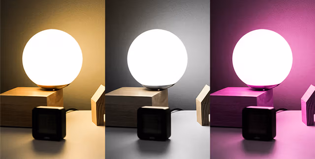 LogiLink WiFi Smart E27 R63 Reflector Bulb with a round, white glass exterior, displayed in three color settings: warm yellow, cool white, and vibrant purple, on a wooden base.